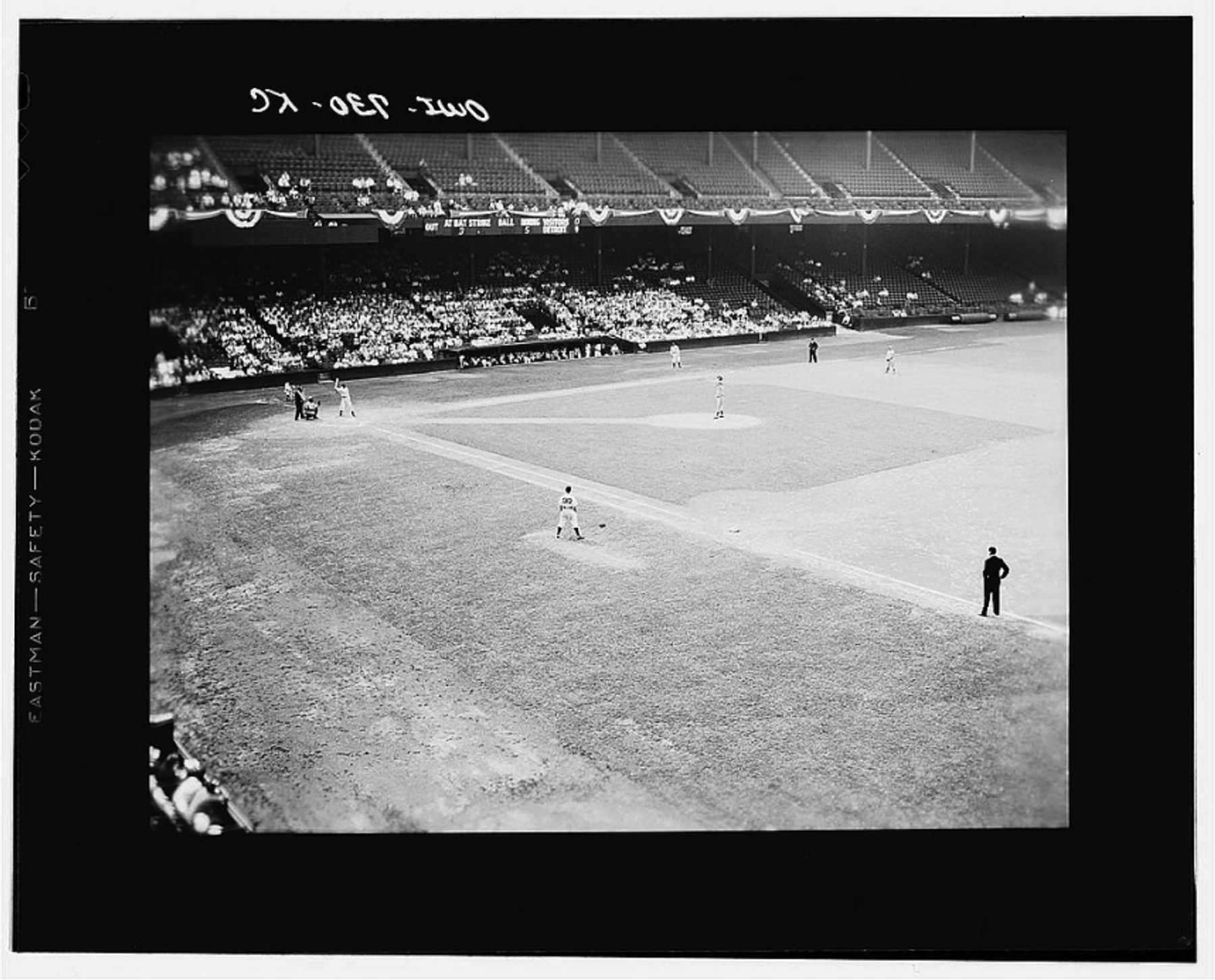 A black and white photograph of a baseball game in progress at a large stadium with stands partially filled with spectators.