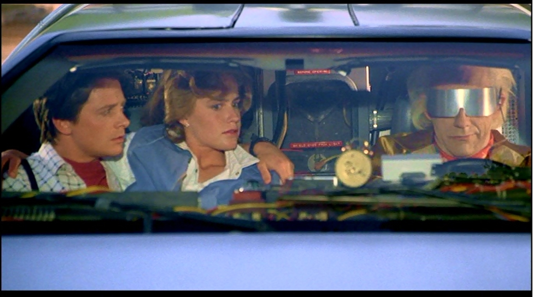Scene from the movie Back to the Future with three people sitting in the front seats of a car.