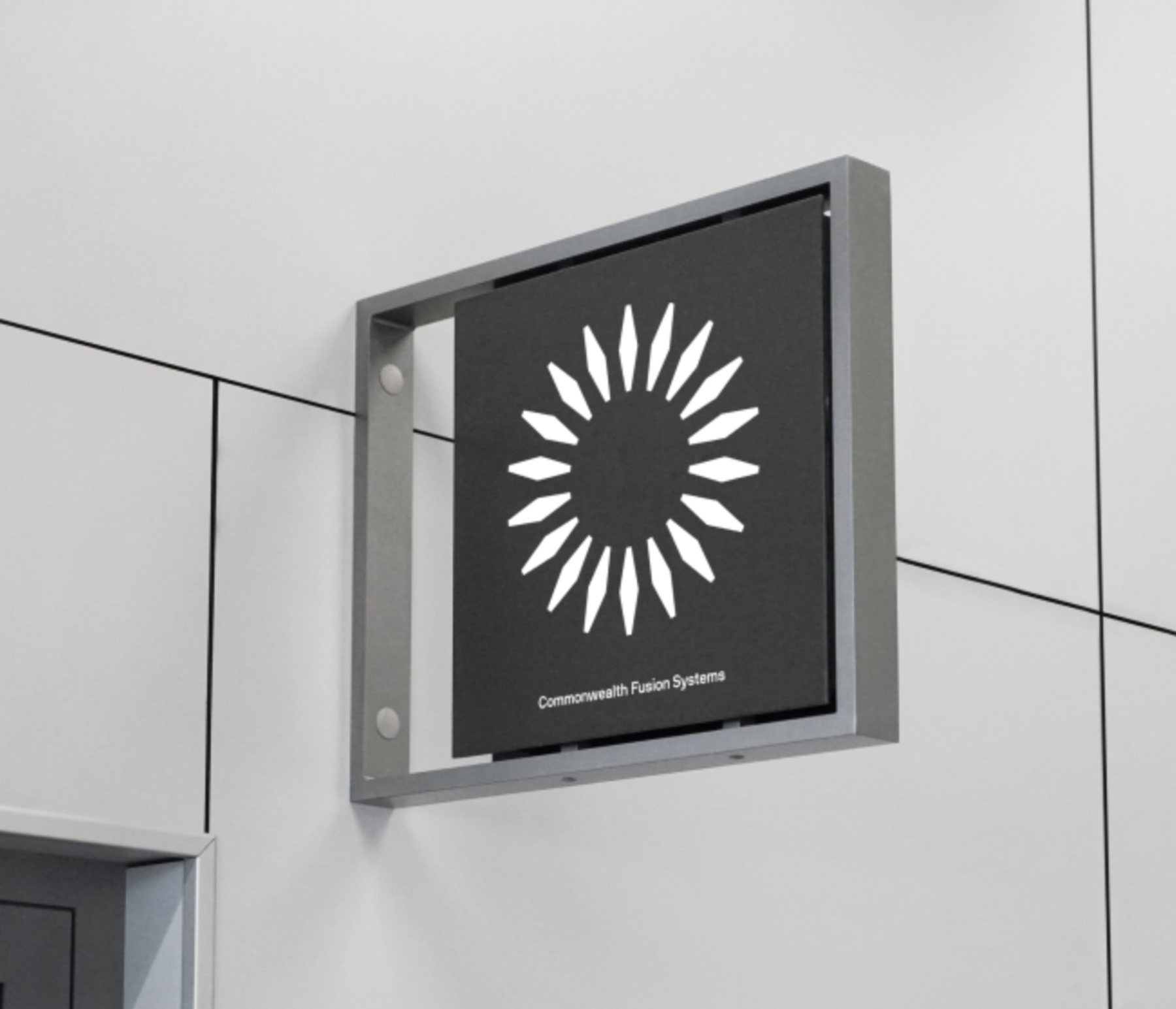 A wall-mounted sign featuring the Commonwealth Fusion Systems logo, a radial design of white shapes resembling sun rays, with the text "Commonwealth Fusion Systems" beneath it.