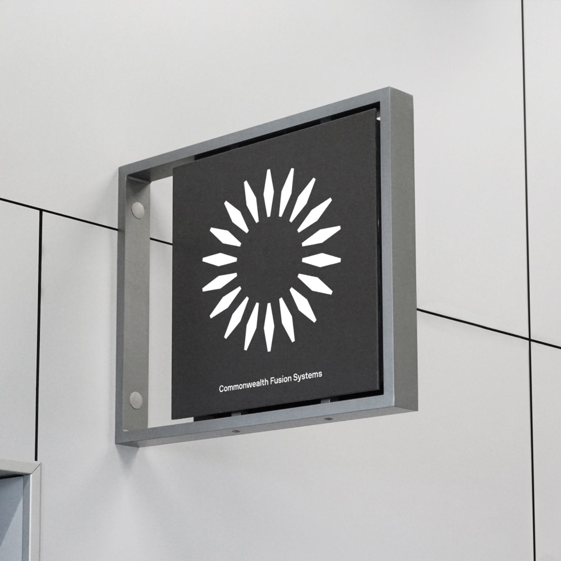 A square sign with the Commonwealth Fusion Systems logo is mounted on a wall.