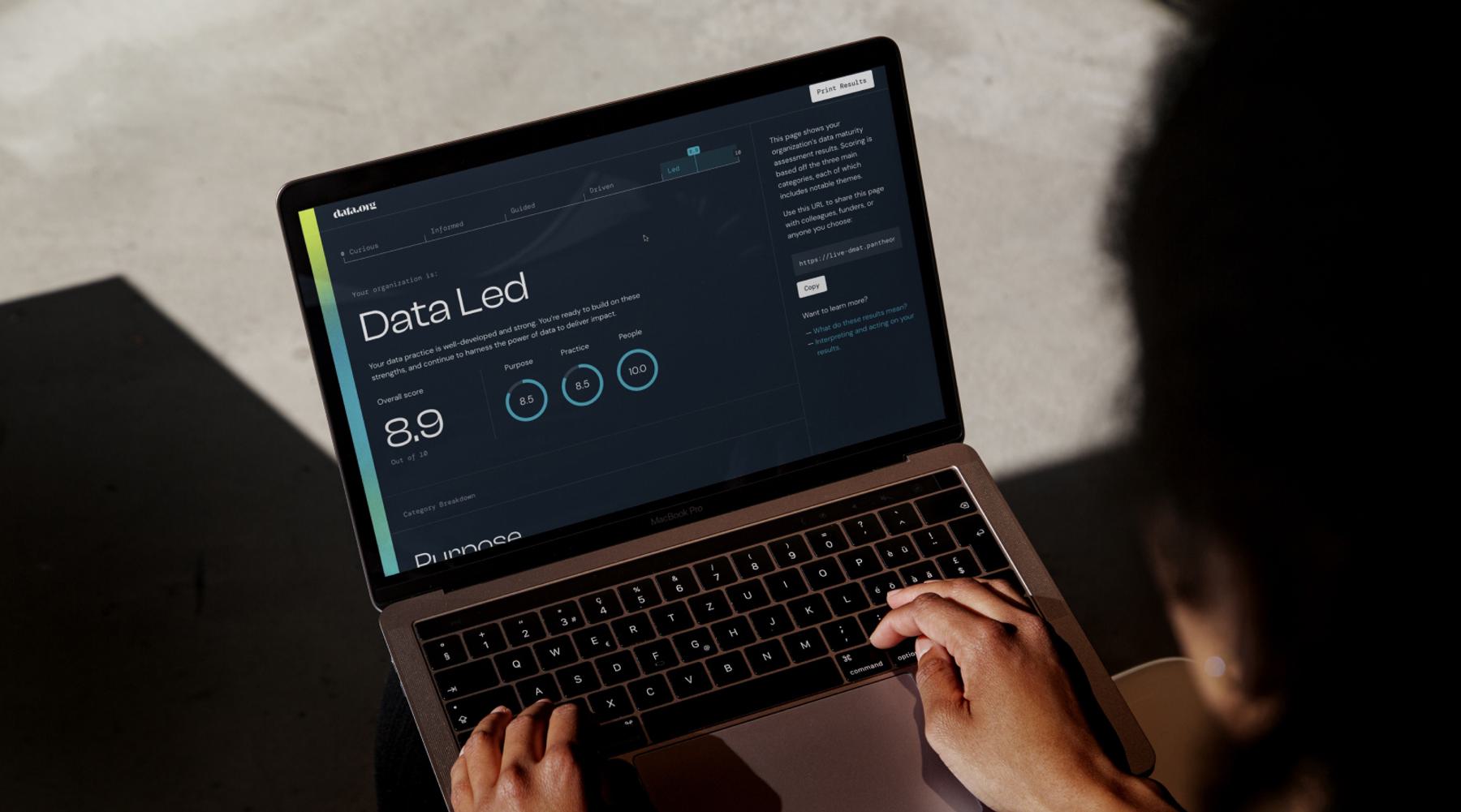 A person is working on a laptop, viewing a dark-themed dashboard on the data.org website with the heading "Data Led."