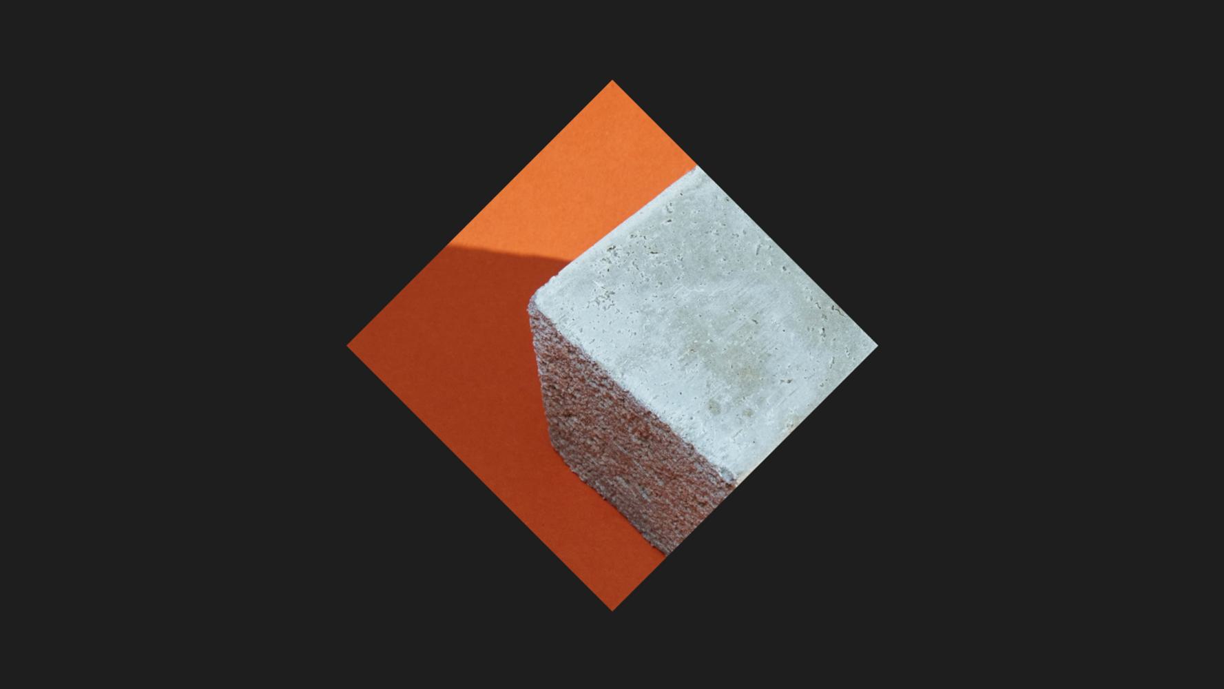 A cement cube with a rough texture, partially illuminated, is placed at an angle against a vibrant orange background.