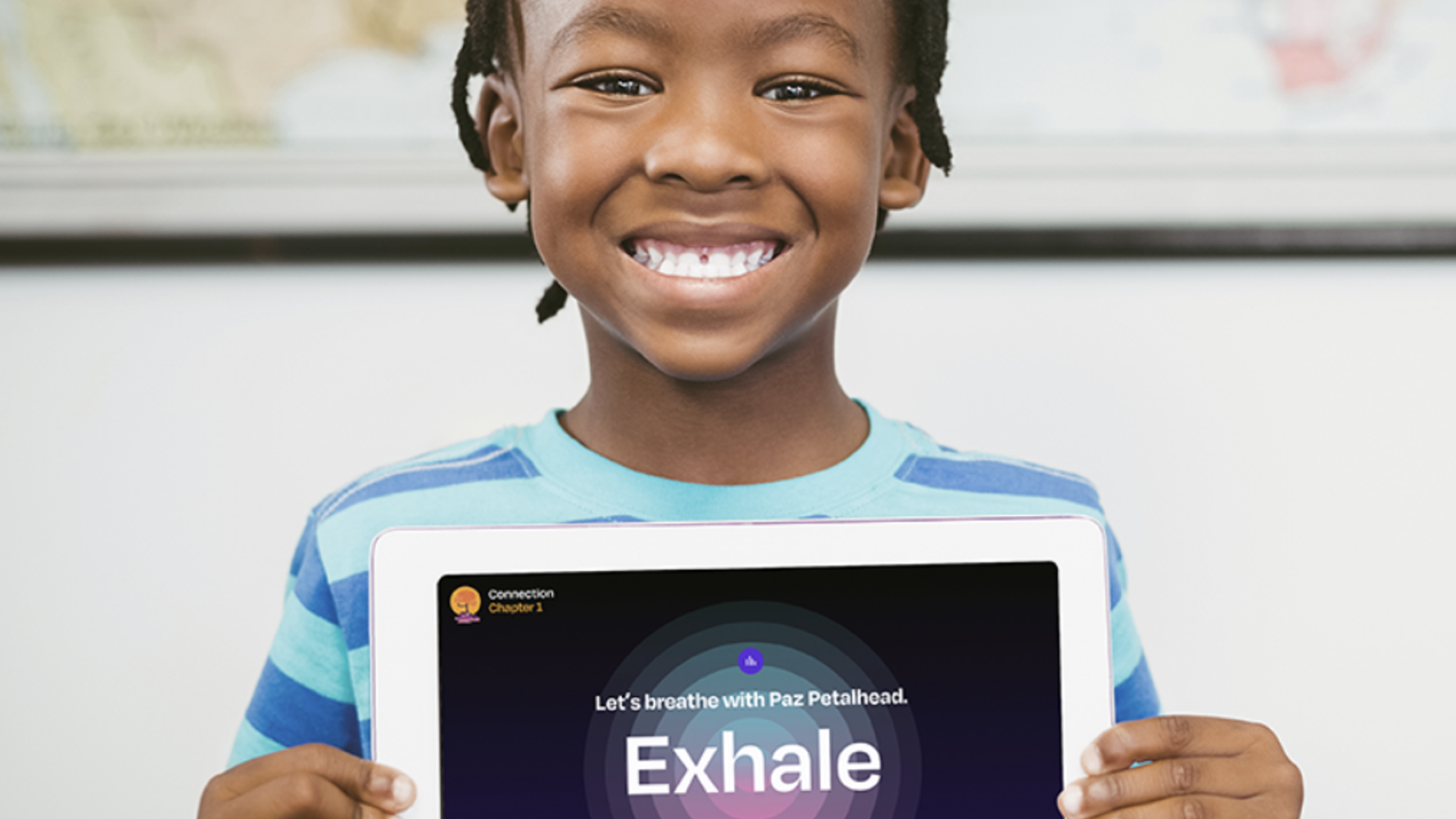 A smiling child holds up a tablet displaying a breathing exercise app. The screen shows, "Let's breathe with Paz" and "Exhale".