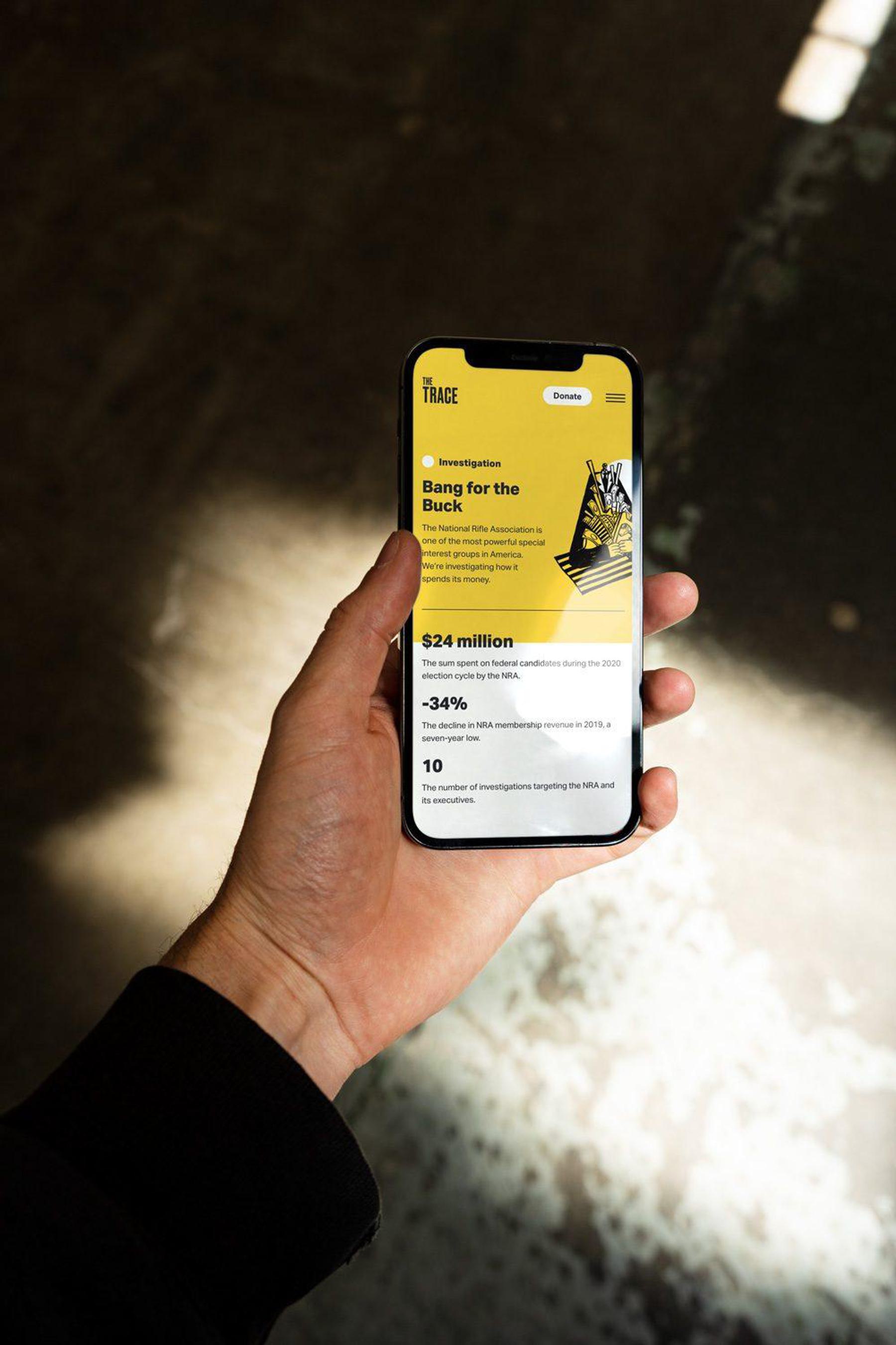 A person holds a smartphone displaying a document about an investigation titled "Bang for the Buck." from the Trace website.